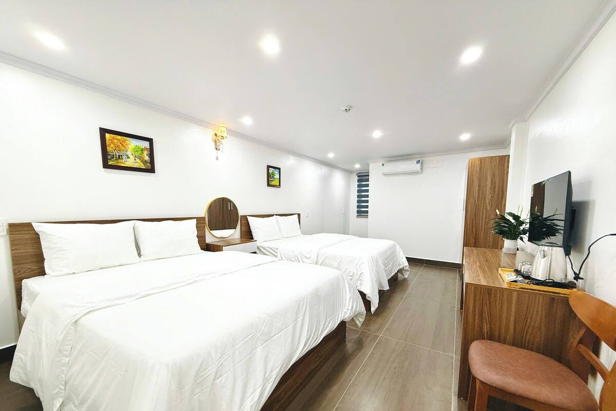 A hotel room with two beds, a desk with a chair, a TV, and a small plant.