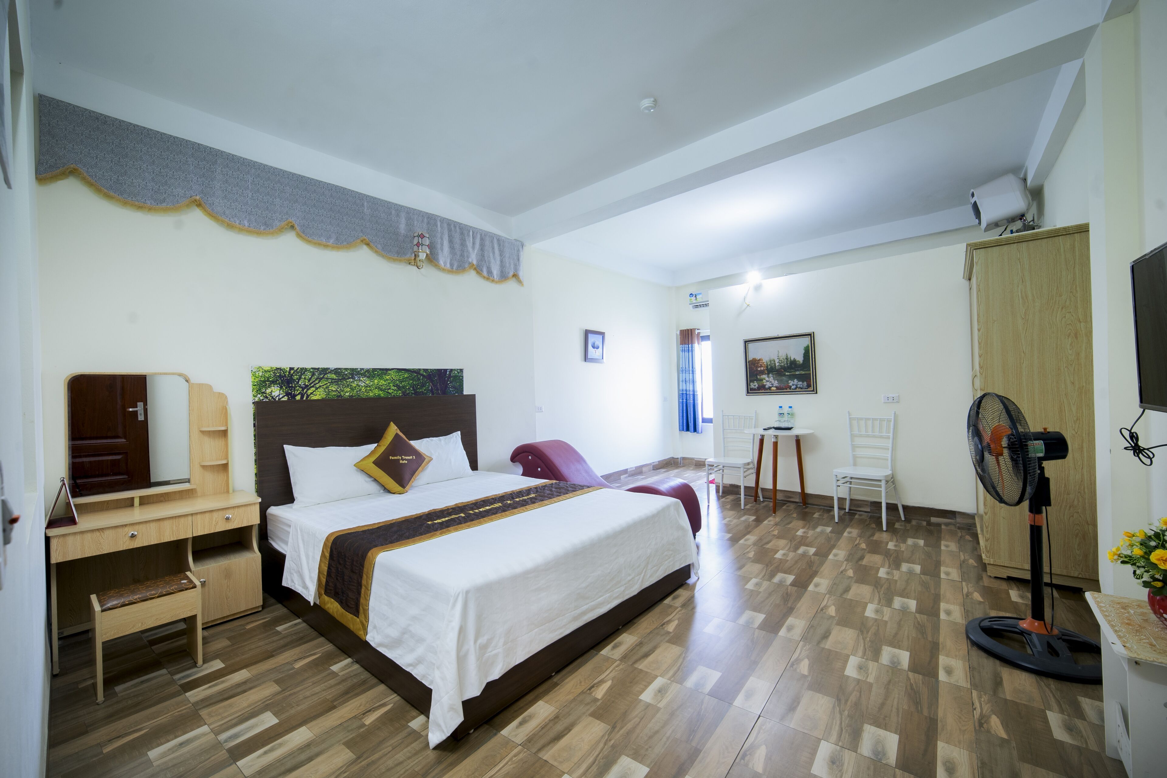 Quarto de hotel com cama, escrivaninha, cadeira e um ventilador.