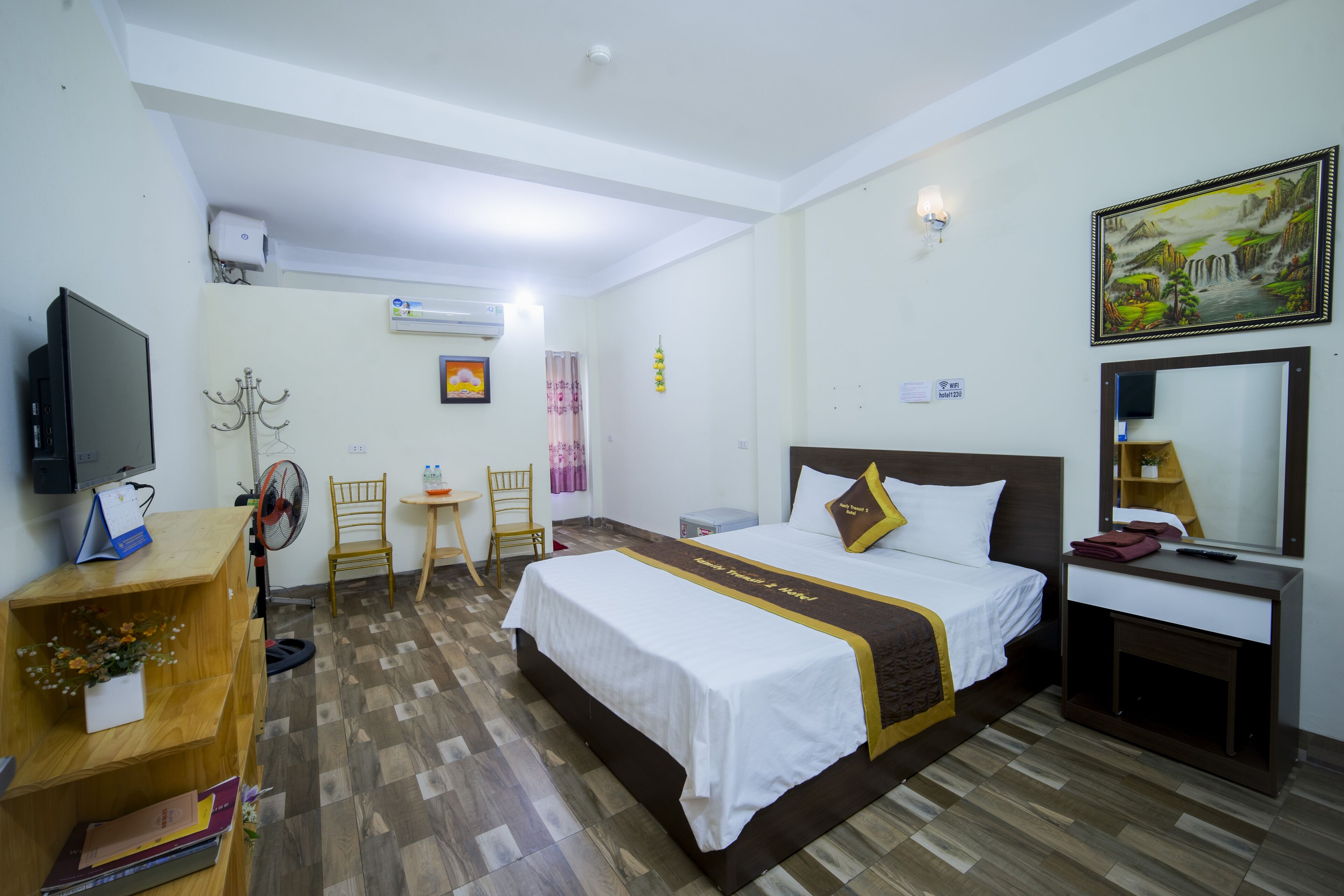 A hotel room with a bed, a desk, a chair, a TV, and a painting on the wall.