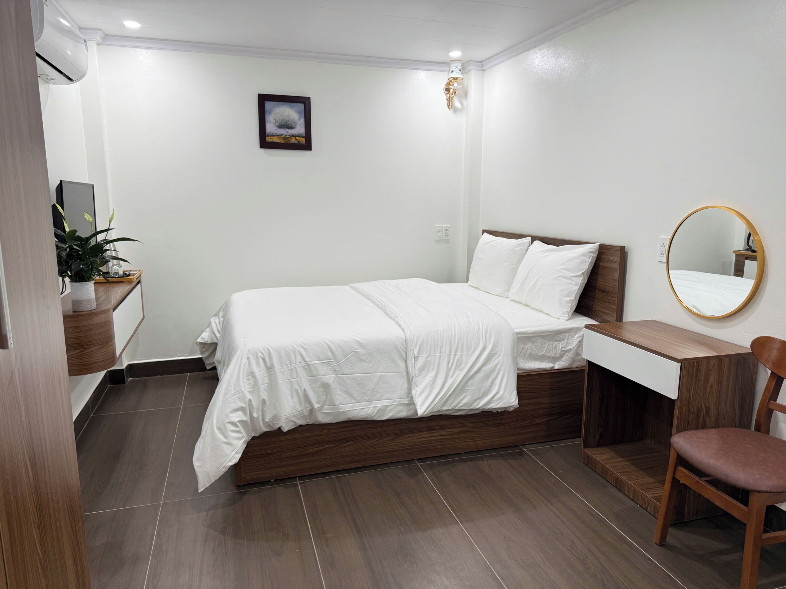A bedroom with a bed, a desk, a chair, a mirror, and a wall-mounted air conditioner.