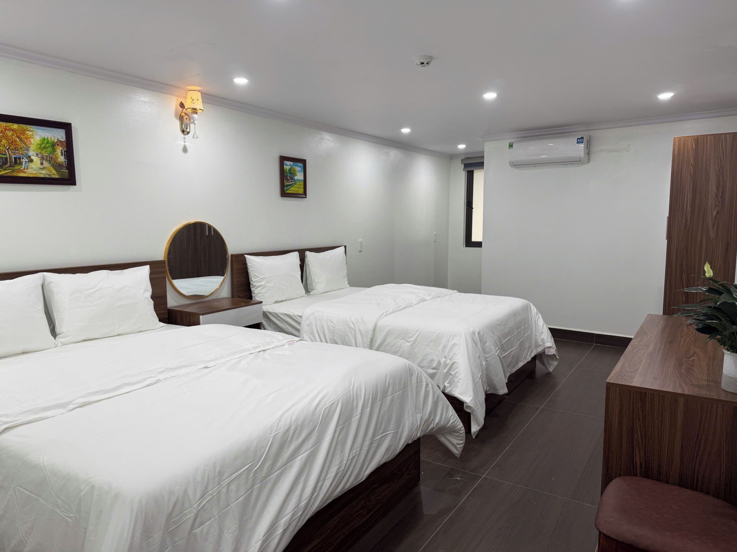 A hotel room with two single beds, a wooden nightstand, a mirror, a wall-mounted air conditioner, and a potted plant.