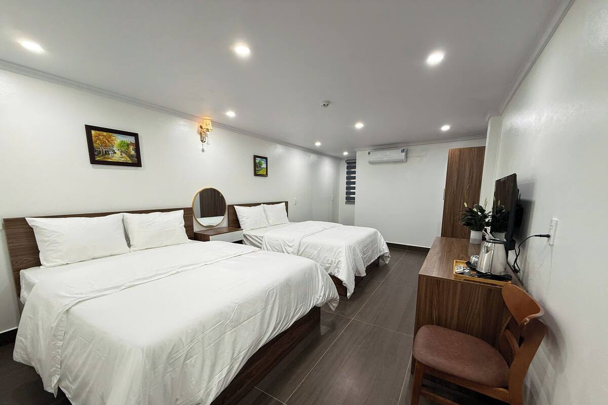 A hotel room with two beds, a desk, a chair, a television, and a small plant.