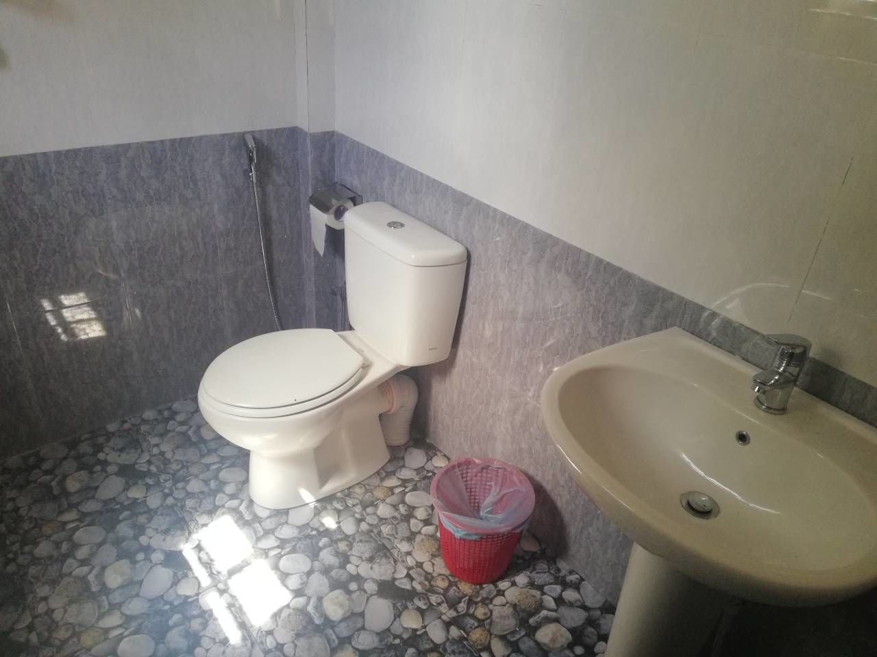 A bathroom with a toilet, a sink, and a trash bin.