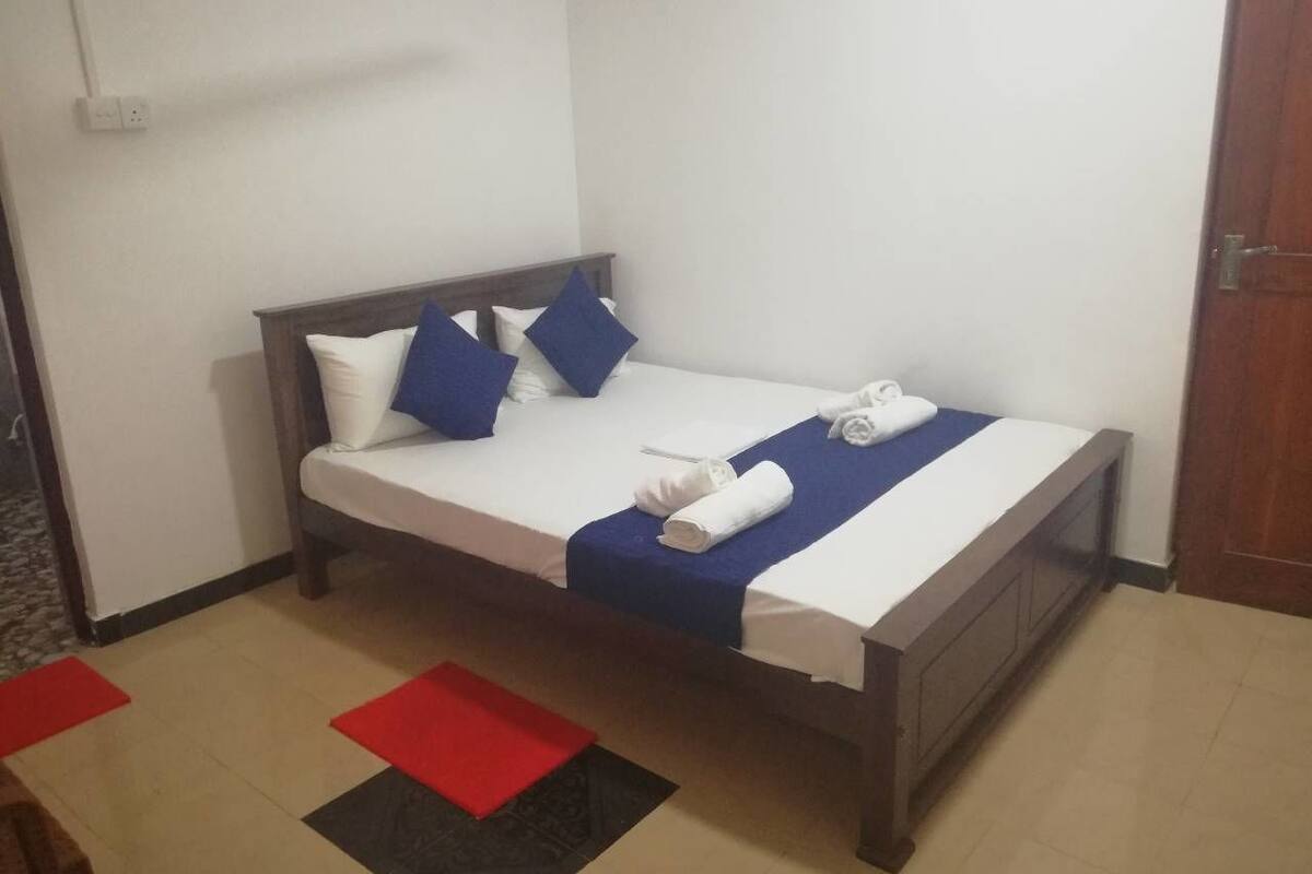 A single bed with a wooden frame, white bedding, blue and white pillows, and a rolled white towel.