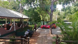 A covered outdoor seating area with a brick wall, a metal roof, and a paved walkway. - N.L.I. Guest House (Habarana)