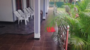 A covered outdoor seating area with white plastic chairs and a tiled floor. - N.L.I. Guest House (Habarana)