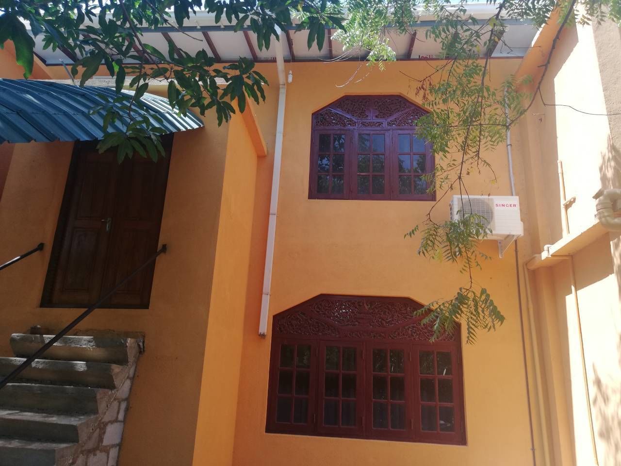 A two-story building with a yellow facade, a wooden door, and a staircase leading to the upper floor.