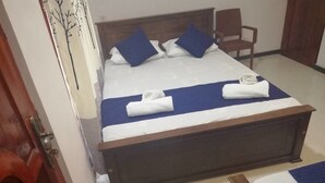 A neatly made bed with blue and white bedding, a wooden headboard, and a chair beside it. - N.L.I. Guest House (Habarana)