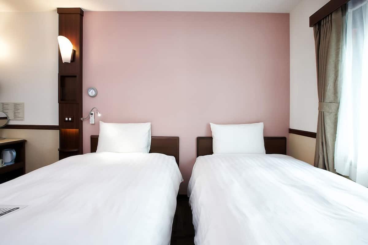 A hotel room with two beds, a nightstand, a clock, and a wall-mounted light.