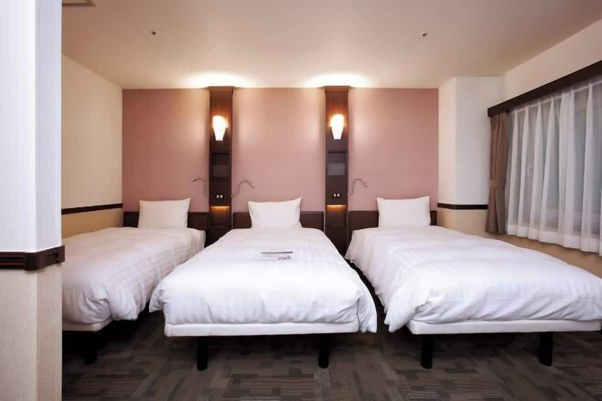 A hotel room with three single beds aligned against a wall with built-in lighting.