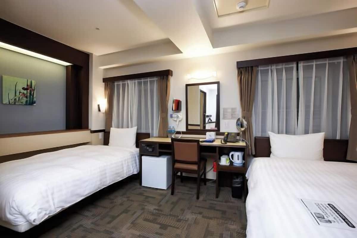A hotel room with two beds, a desk, a chair, a coffee maker, and a mirror.