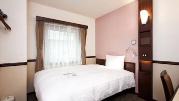 A hotel room with a large bed, a bedside table, a wall-mounted lamp, and a window with curtains.