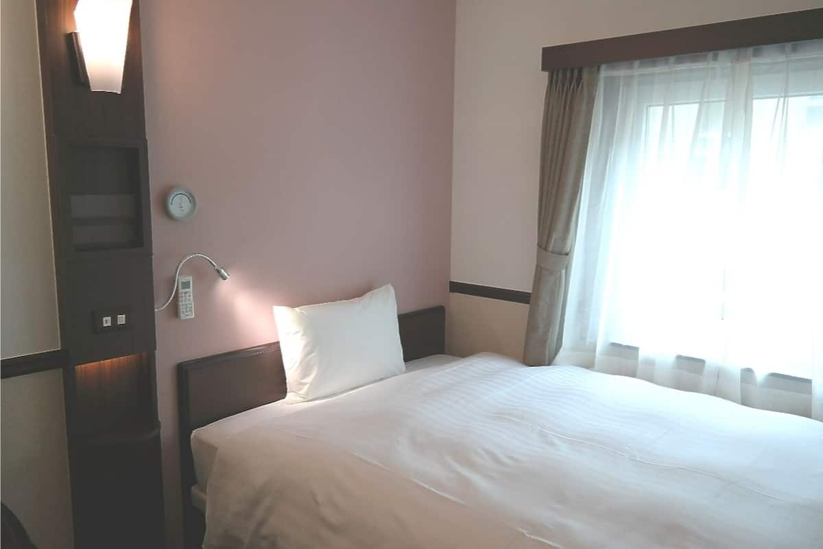 A hotel room with a bed, a bedside telephone, a wall clock, and a window with curtains.