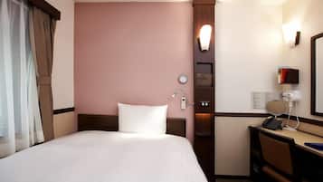 A hotel room with a bed, a desk with a phone and a mirror, a clock, and a wall-mounted light.