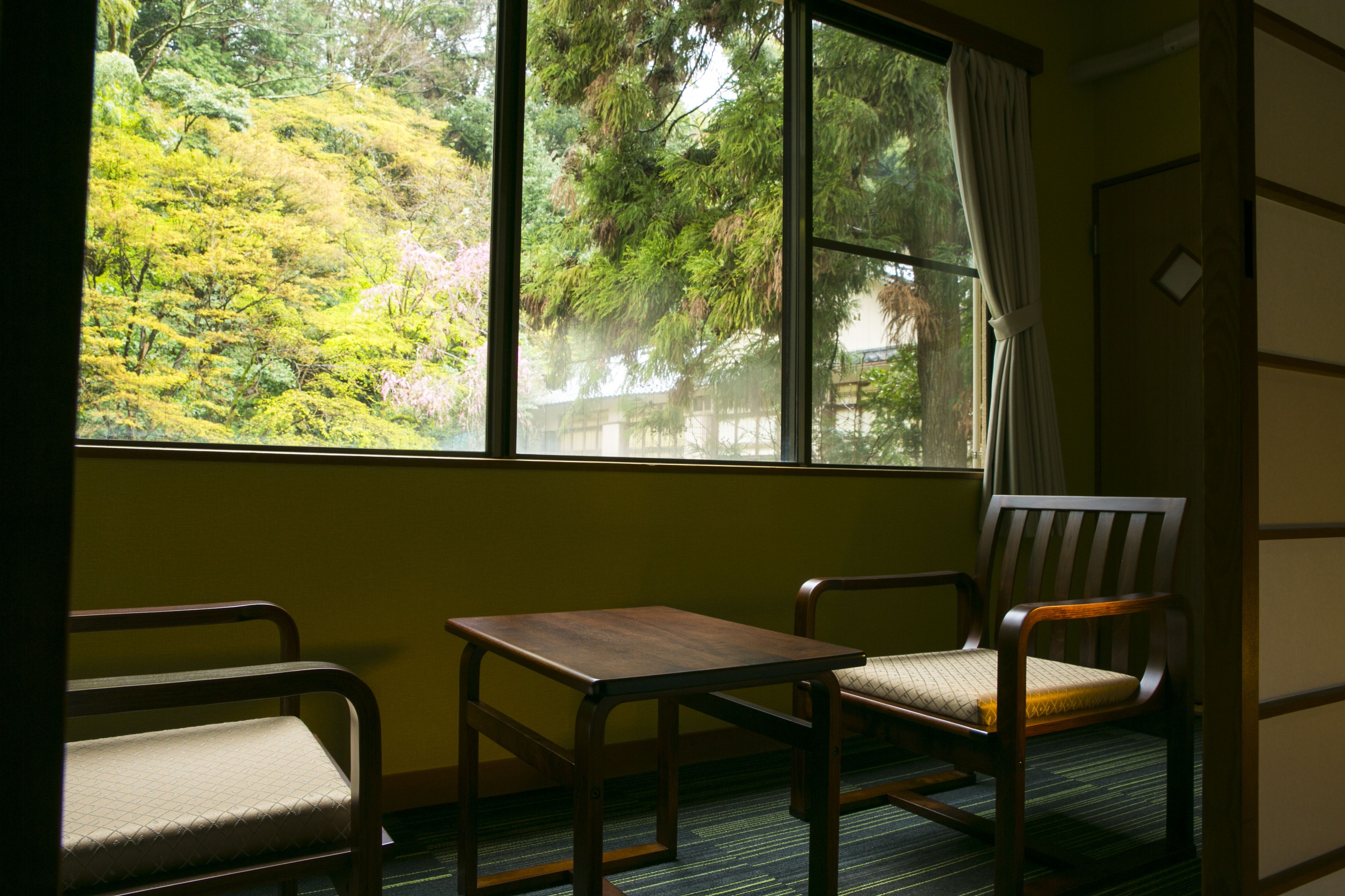 A room with a large window, two chairs, a small table, and a bed.