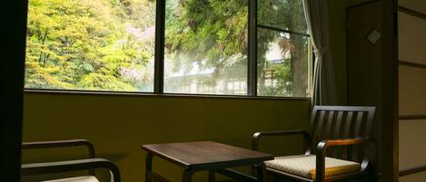A room with a large window, two chairs, a small table, and a bed.