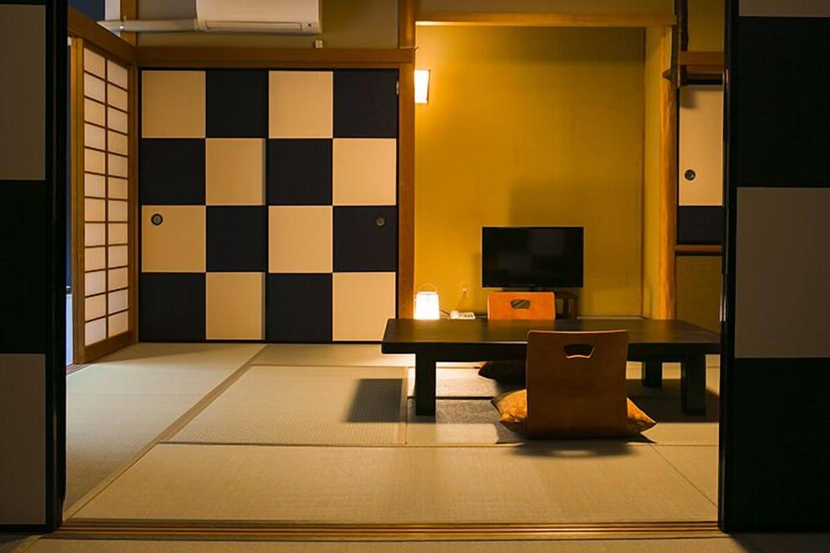 Ein traditioneller japanischer Raum mit Tatami-Boden, einem Fernseher, einem Tisch und einer Couch.