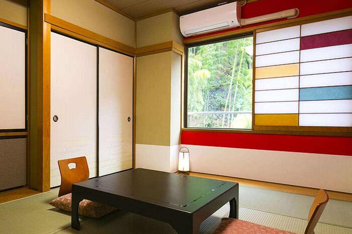 Ein traditioneller japanischer Raum mit Tatami-Bodenbelag, einem niedrigen Tisch, einem Stuhl und einer Schiebetür.