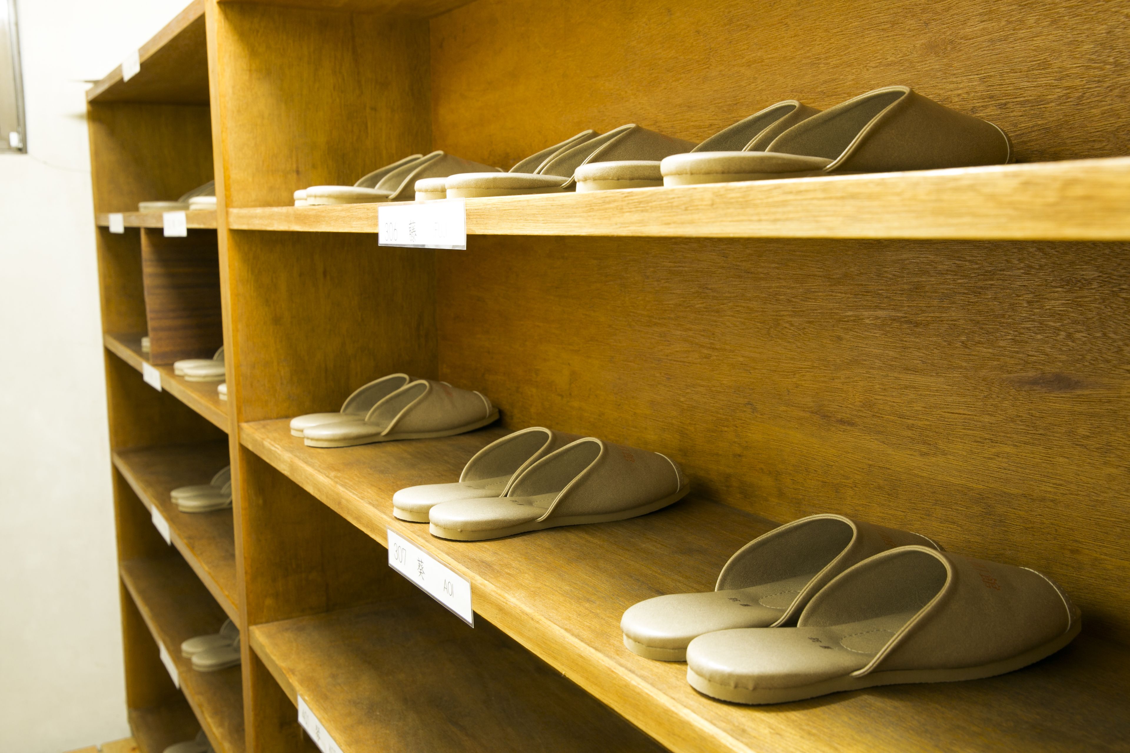 A wooden shelf with multiple pairs of beige slippers.
