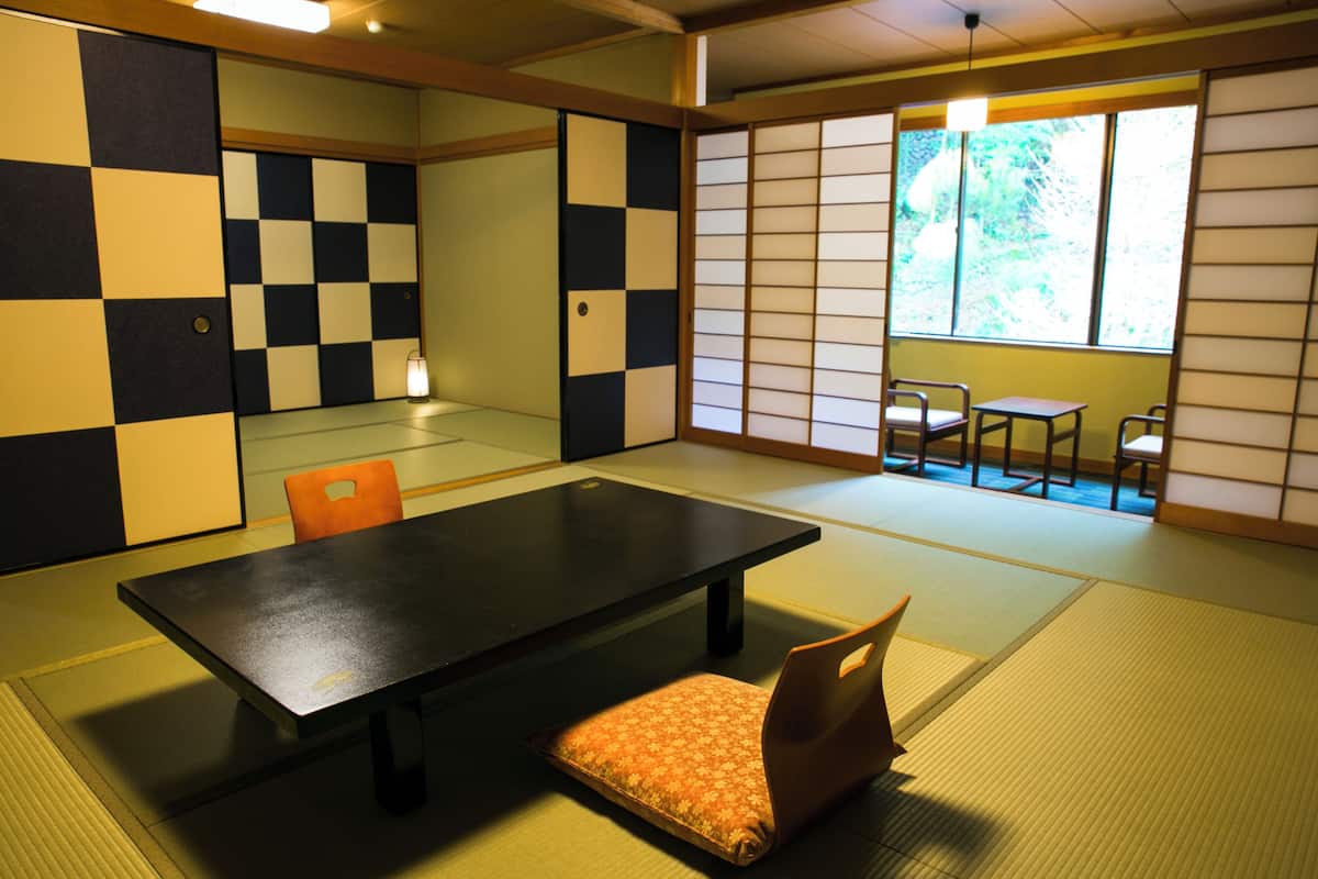 Ein Raum mit Tatami-Böden, einem niedrigen Tisch, Kissen und einer Schiebetür.
