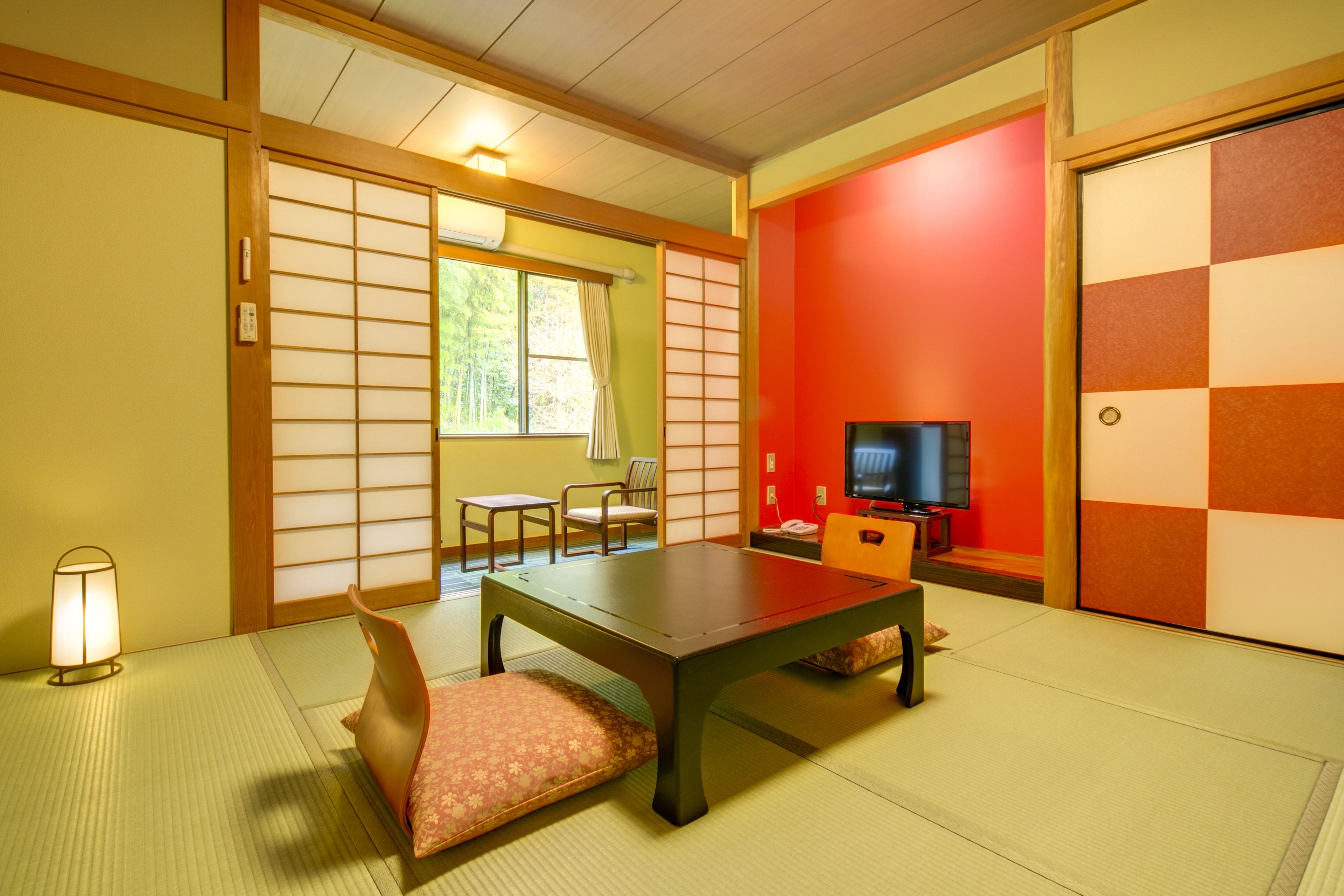A traditional Japanese room with tatami flooring, a low table, a sofa, a television, and sliding doors.