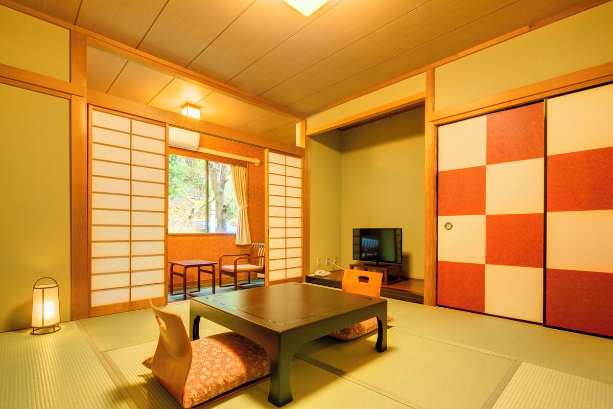 Ein traditioneller japanischer Raum mit Tatami-Böden, einem niedrigen Tisch, einem Fernseher und Schiebetüren.