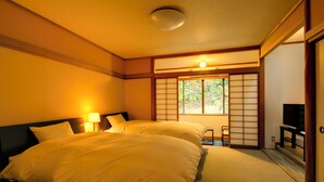 A hotel room with two beds, a TV, a sliding door, and a window with a view of greenery. - Yumoto Komachikan (Yugawara)