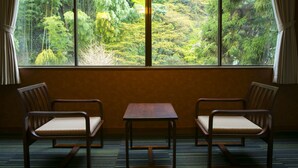 A room with a large window offering a view of a forest. There are two wooden chairs and a small table in the room. - Yumoto Komachikan (Yugawara)