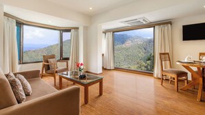 Quarto espaçoso com grande janela e vista para as montanhas, televisão de tela plana na parede e área de jantar com mesa e cadeiras de madeira.