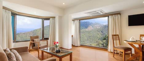 Une chambre spacieuse dotée d’une grande fenêtre offrant une vue sur les montagnes, d’un téléviseur à écran plat fixé au mur et d’un coin repas avec une table et des chaises en bois.