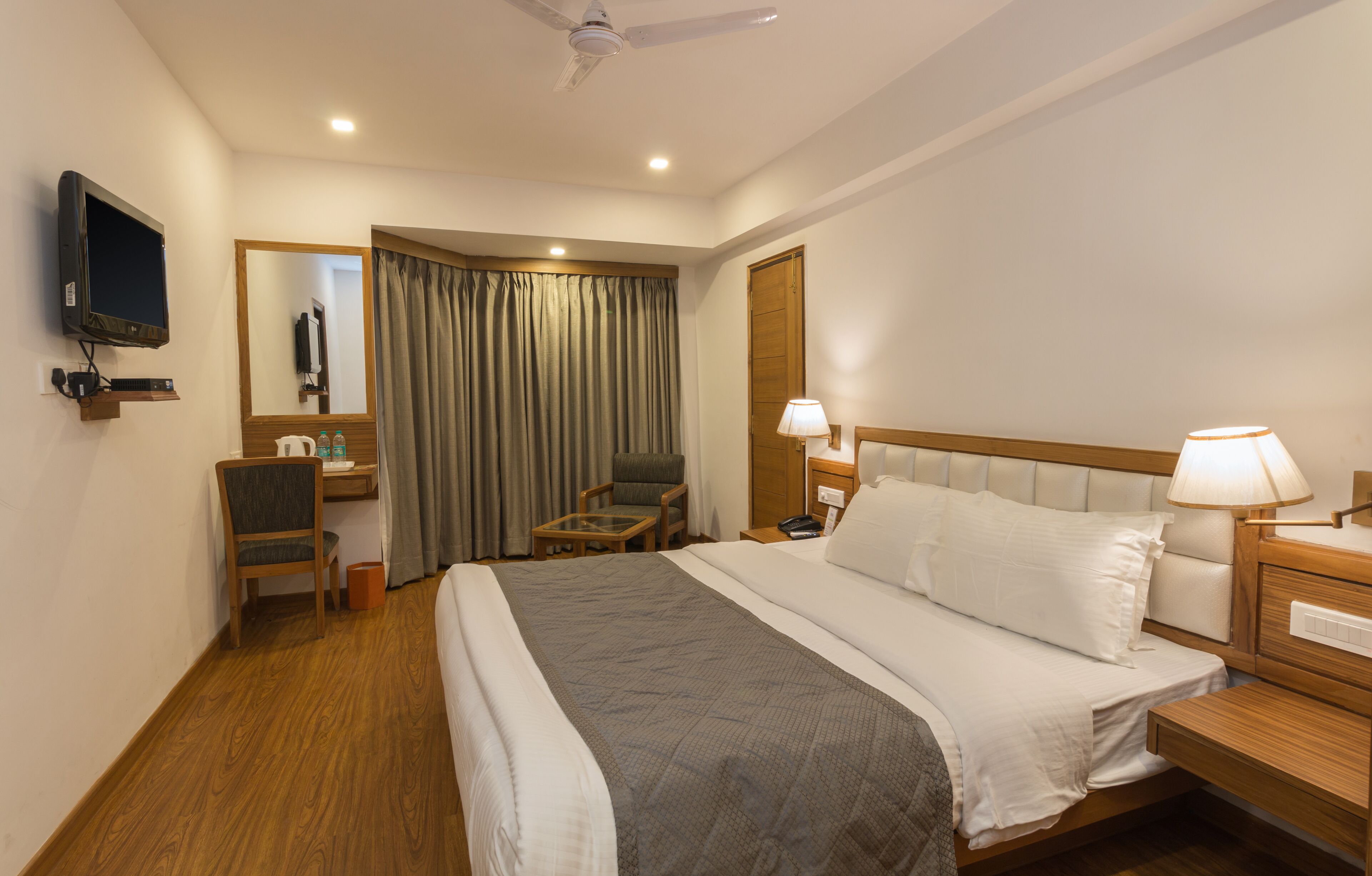 Una habitación de hotel con cama, escritorio, silla, televisor y ventilador de techo.