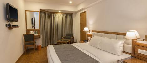 Una habitación de hotel con cama, escritorio, silla, televisor y ventilador de techo.