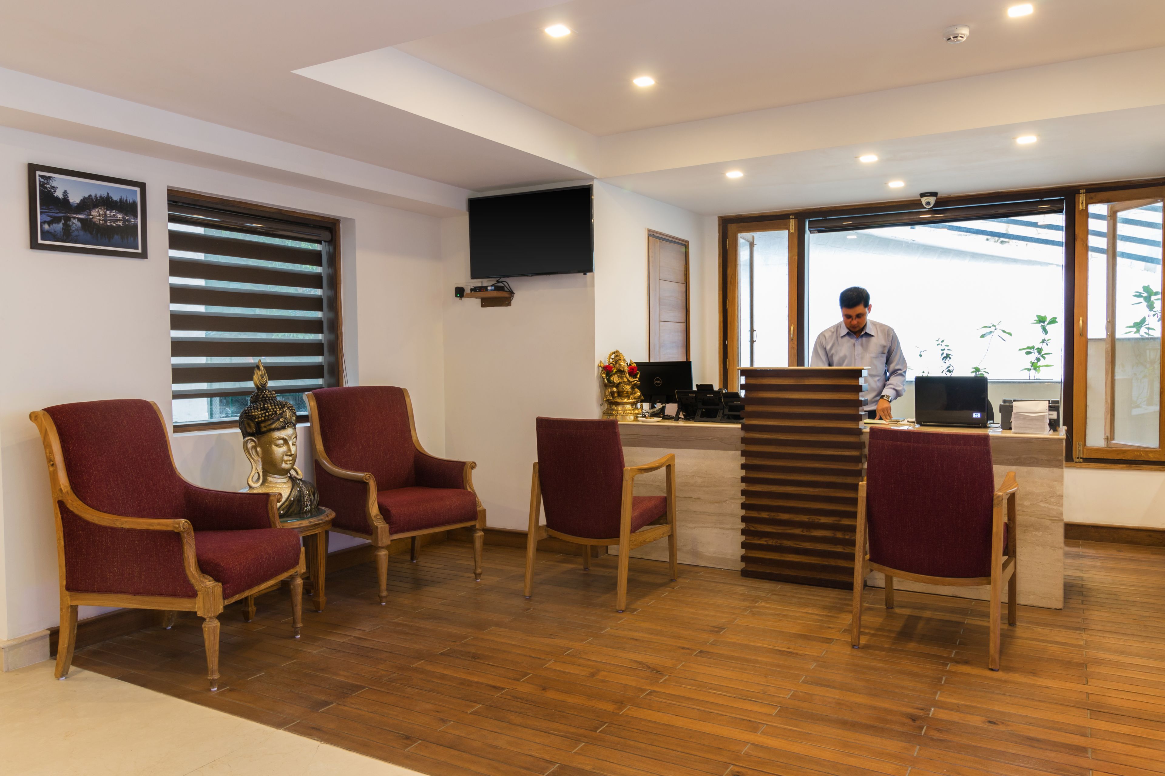 A reception area with a wooden reception desk, a Buddha statue, and a large window with blinds.