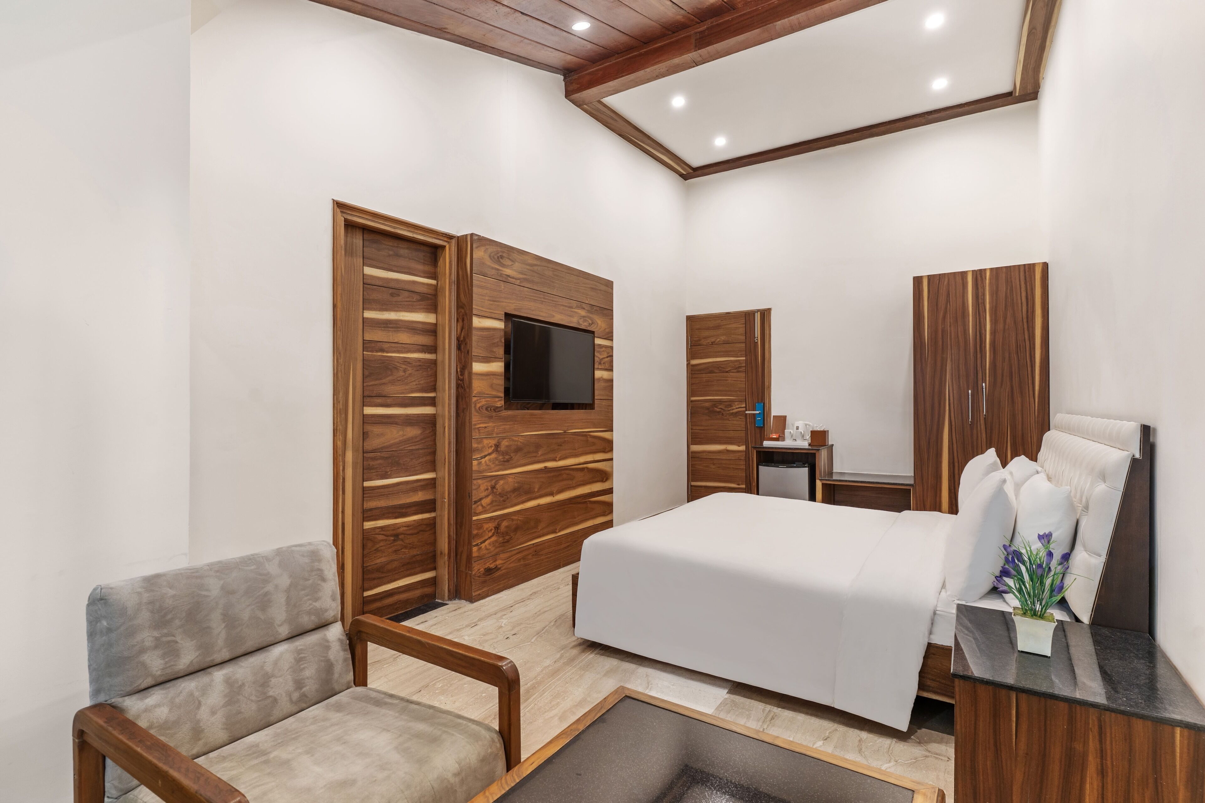 A modern bedroom with a bed, a TV, wooden wardrobes, a seating area, and a small table with a plant.
