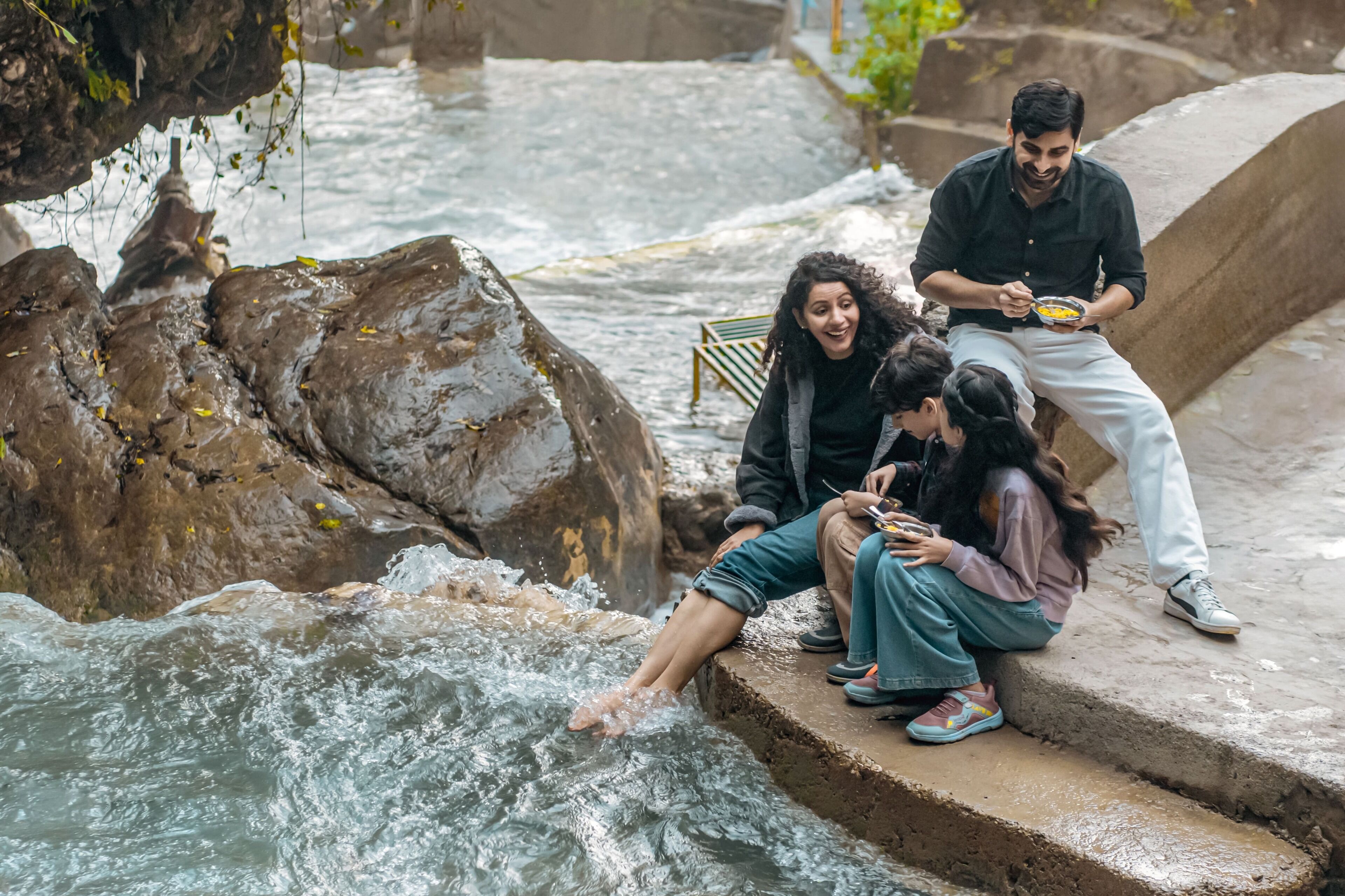 A group of people sitting on stone steps by a flowing river.