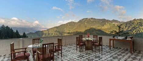 A terrace with a geometric patterned floor, wooden furniture, and a view of a forested mountain range.