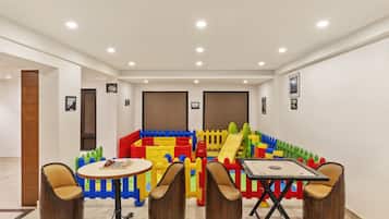 Espaço de recreação com estruturas coloridas e duas mesas redondas com cadeiras.