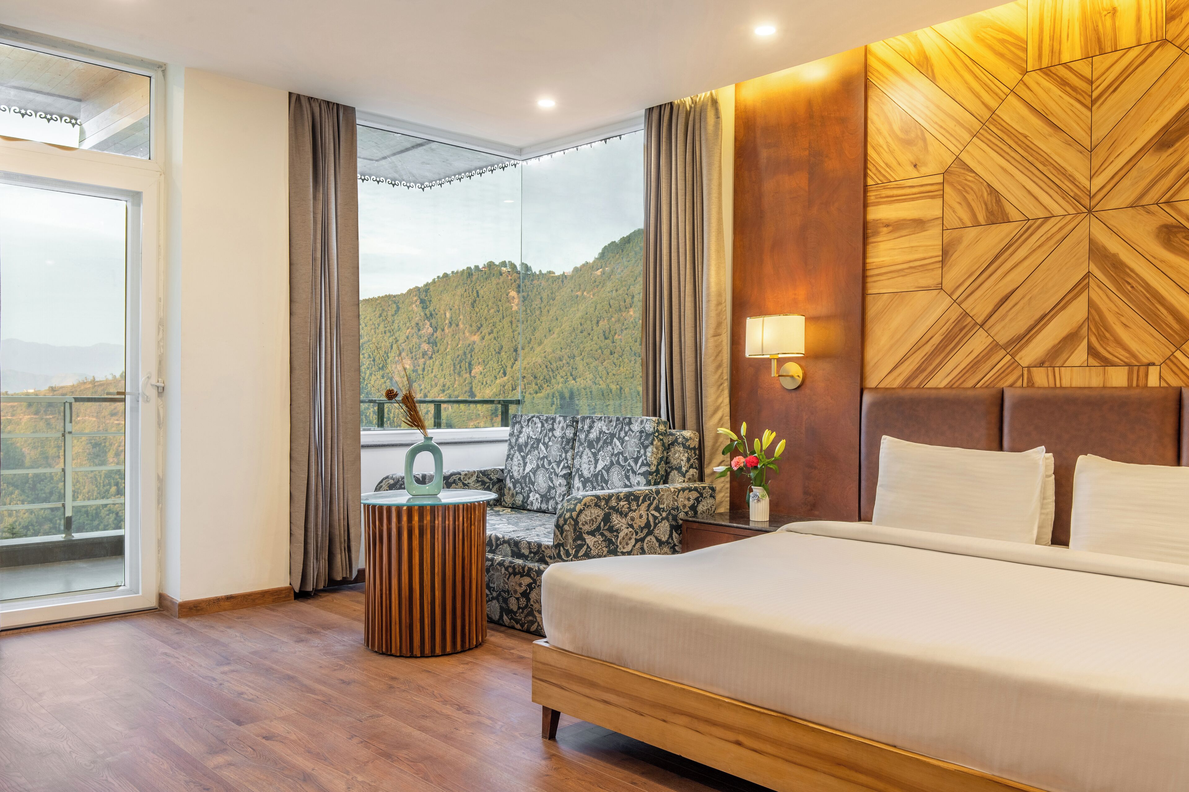 Habitación de hotel con una cama grande, un sofá, una mesita auxiliar y vistas a un paisaje montañoso.