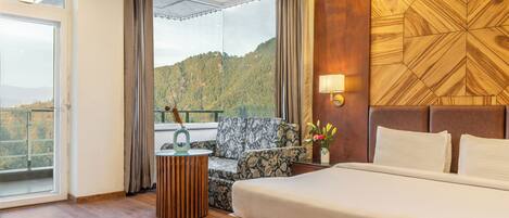 Habitación de hotel con una cama grande, un sofá, una mesita auxiliar y vistas a un paisaje montañoso.