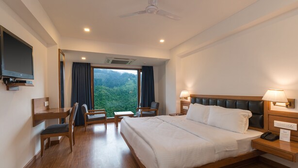 Quarto de hotel com uma cama grande, uma escrivaninha, uma cadeira, uma televisão e vista para o exterior.