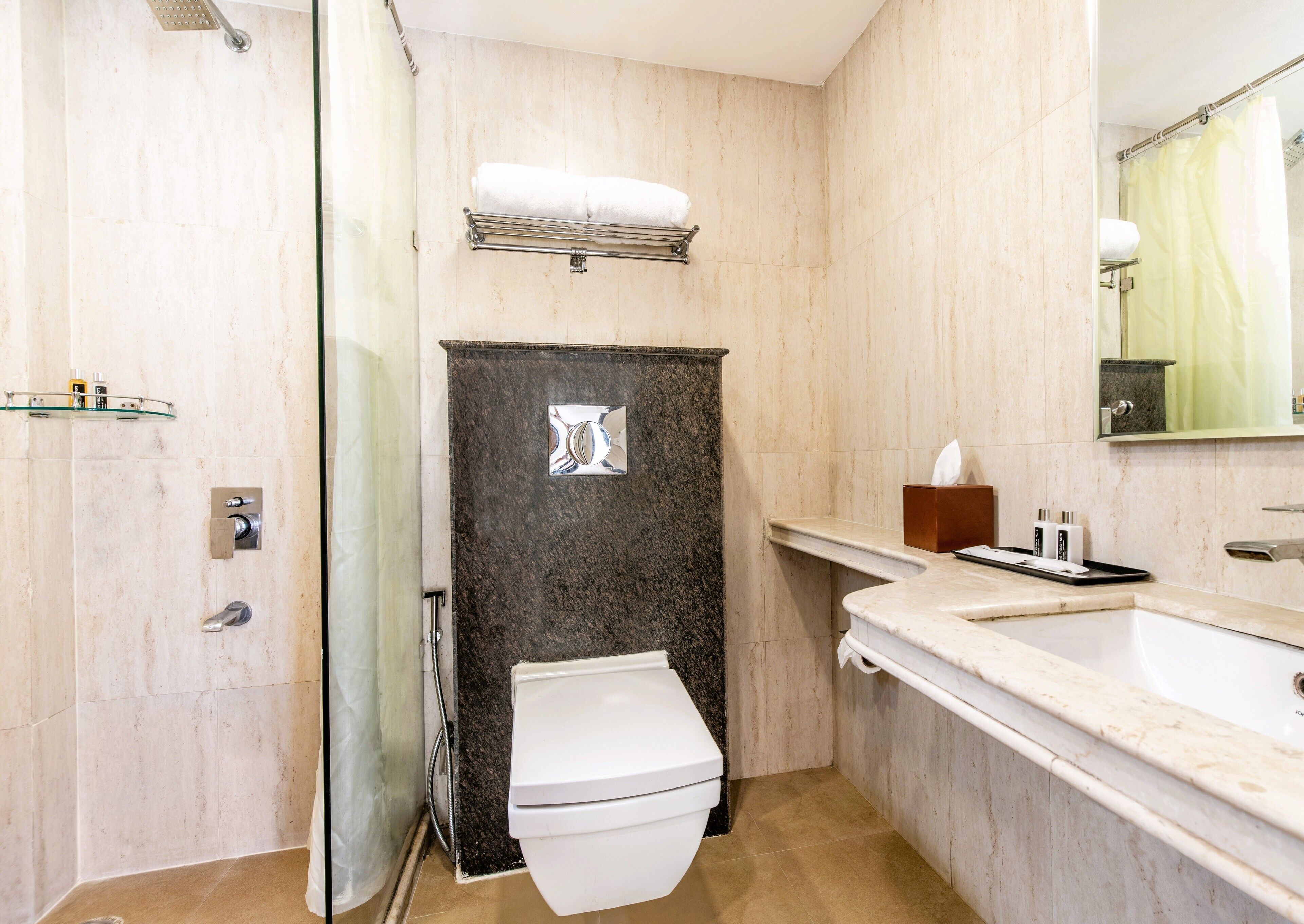 A modern bathroom with a glass shower enclosure, a white toilet, a marble sink, and a mirror above the sink.