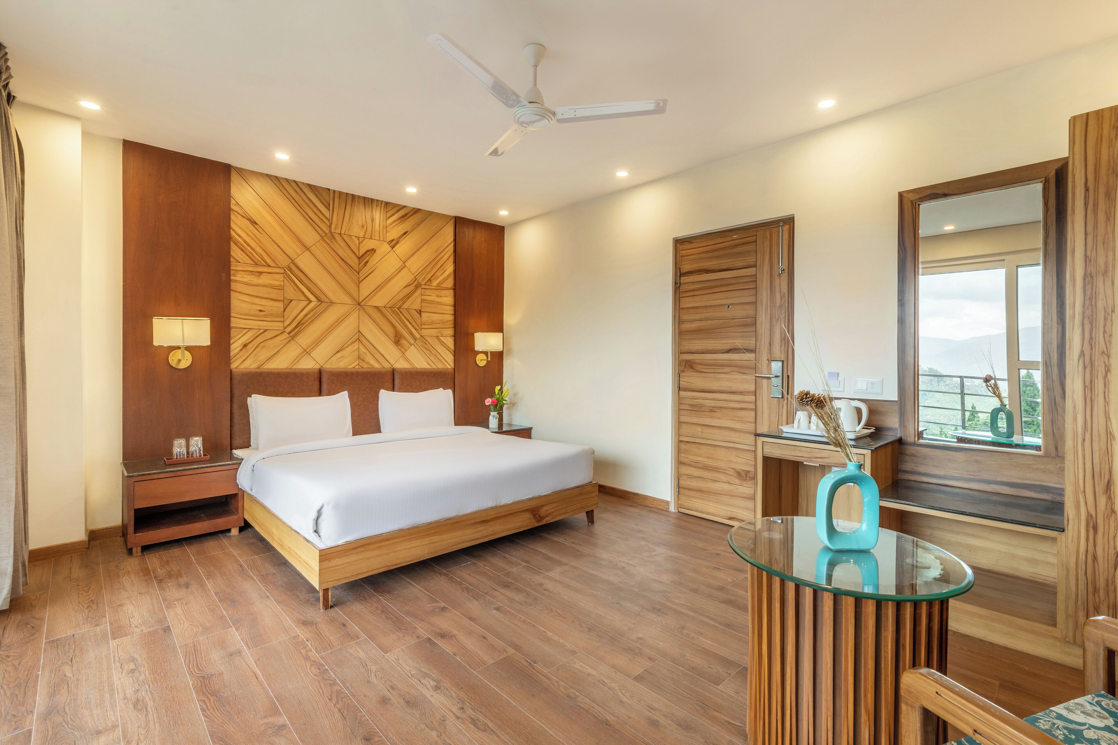 A modern bedroom with a wooden headboard, a glass table, and a view of the outdoors.