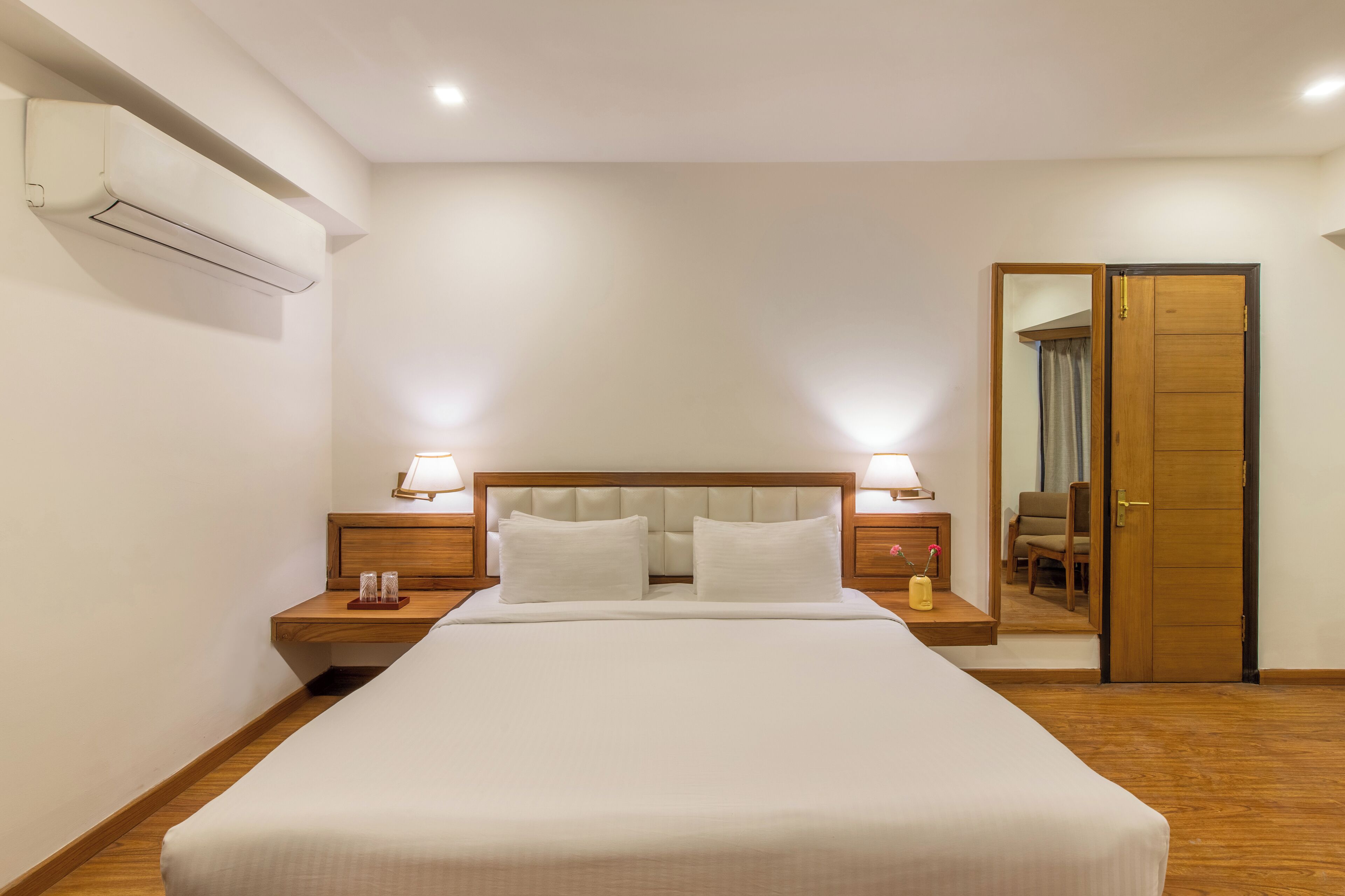 A neatly made bed with a wooden headboard, two bedside lamps, and a small table with a glass and a bottle.