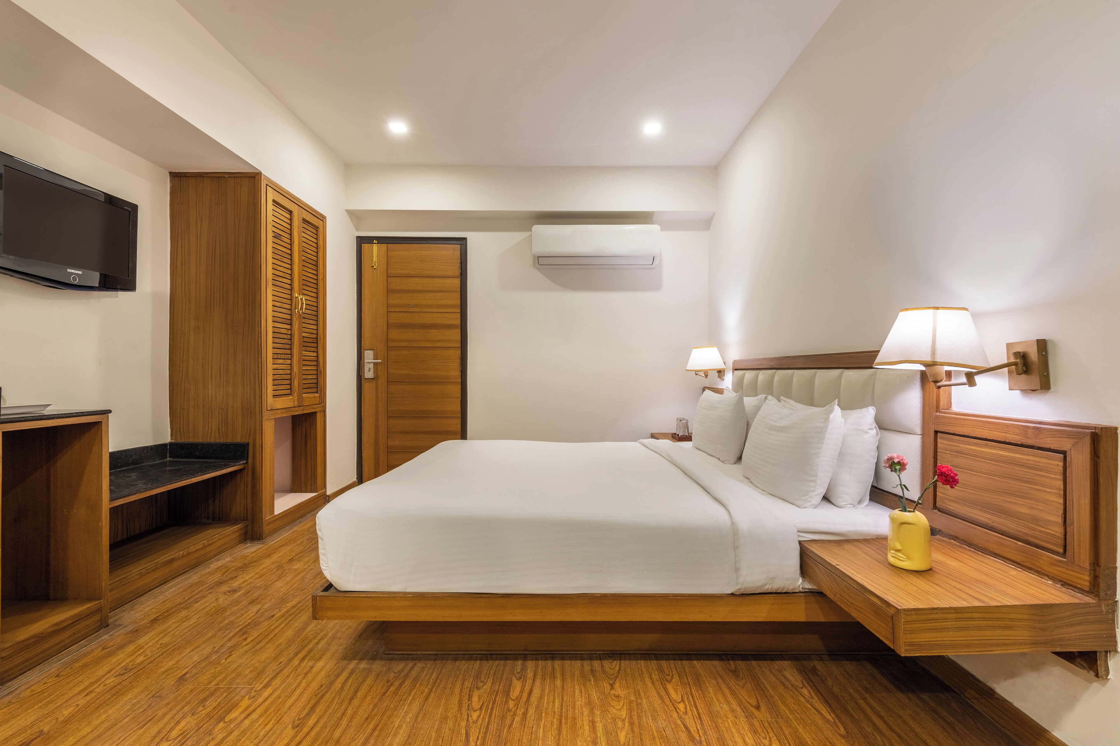 Een moderne slaapkamer met een groot bed, een houten garderobe, nachtkastjes, een televisie en een airconditioner.