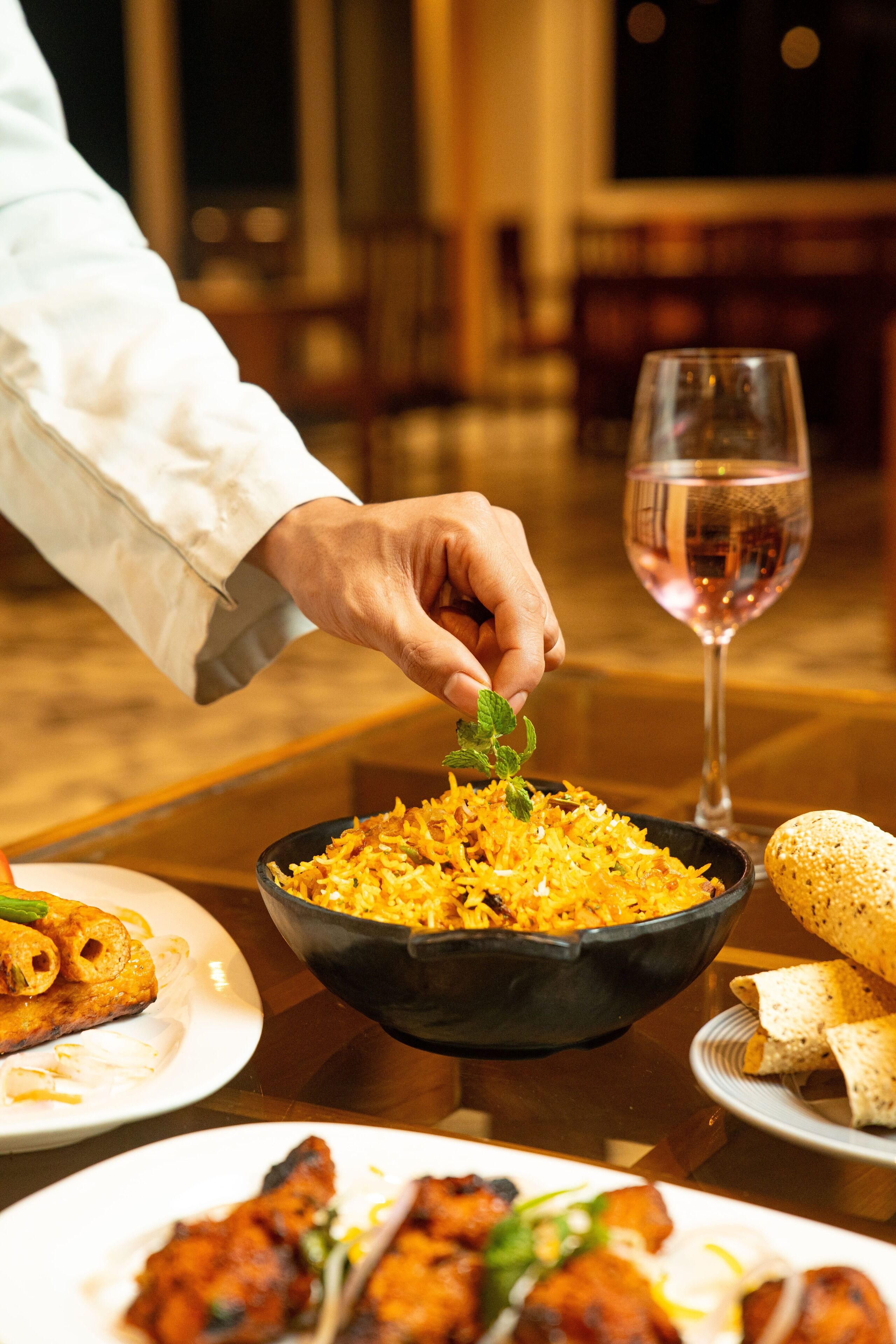 A dining table with a bowl of rice, a glass of wine, and various dishes.