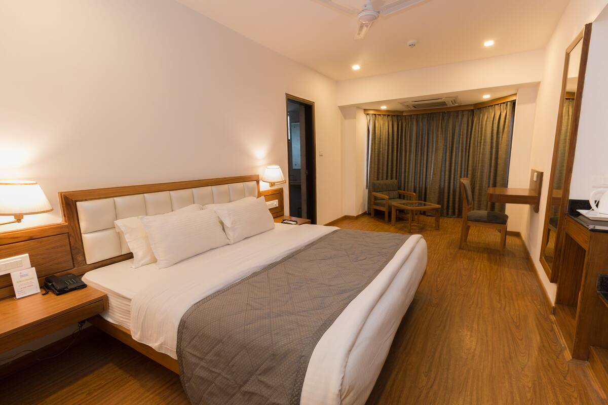 A hotel room with a large bed, bedside tables, a desk, a chair, and a mirror.