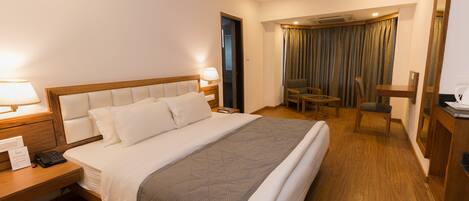 Una habitación de hotel con una cama grande, mesitas de noche, un escritorio, una silla y un espejo.
