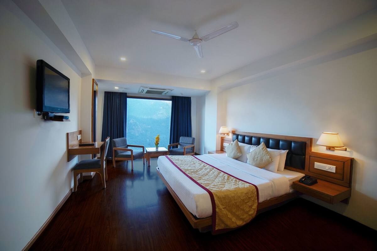 A hotel room with a large bed, a desk, a chair, a television, and a window with curtains.