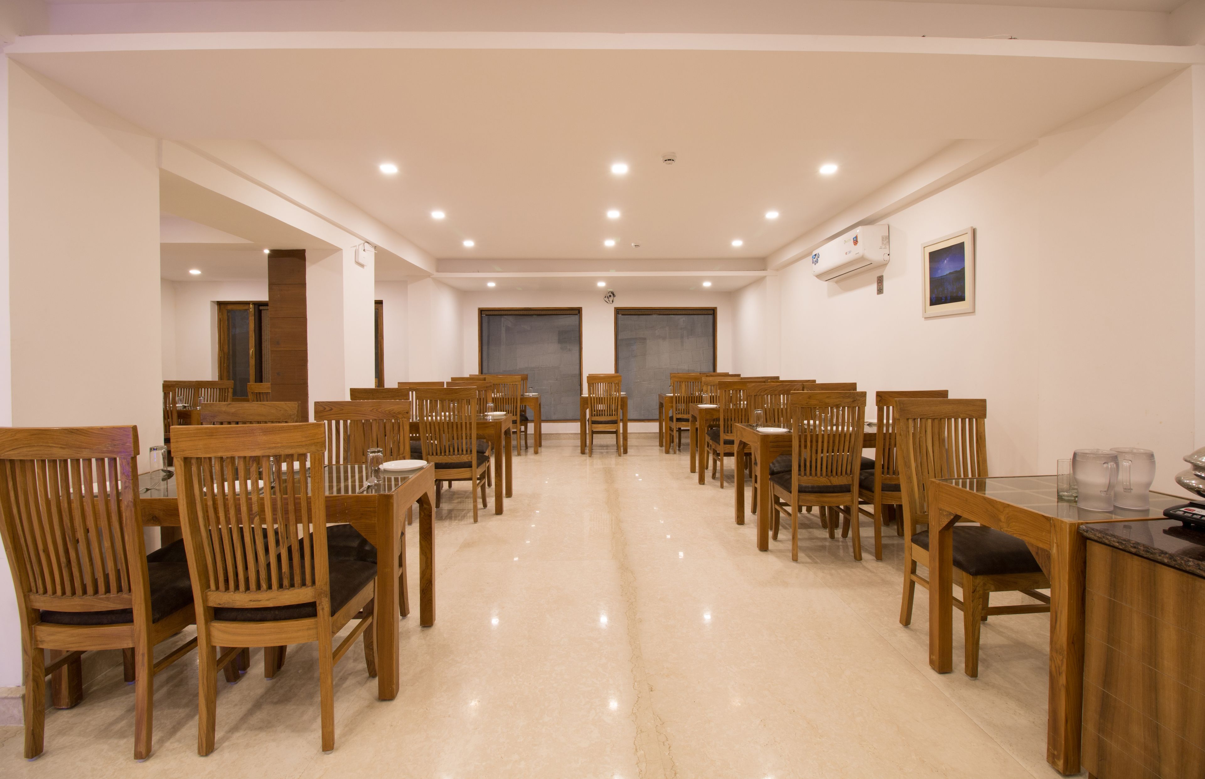 A spacious dining area with multiple wooden tables and chairs, a polished floor, and recessed ceiling lights.