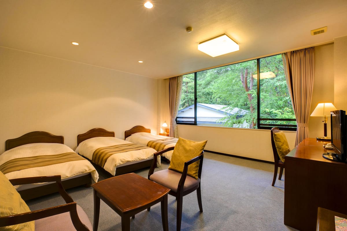 A hotel room with two single beds, a desk, a chair, and a TV.